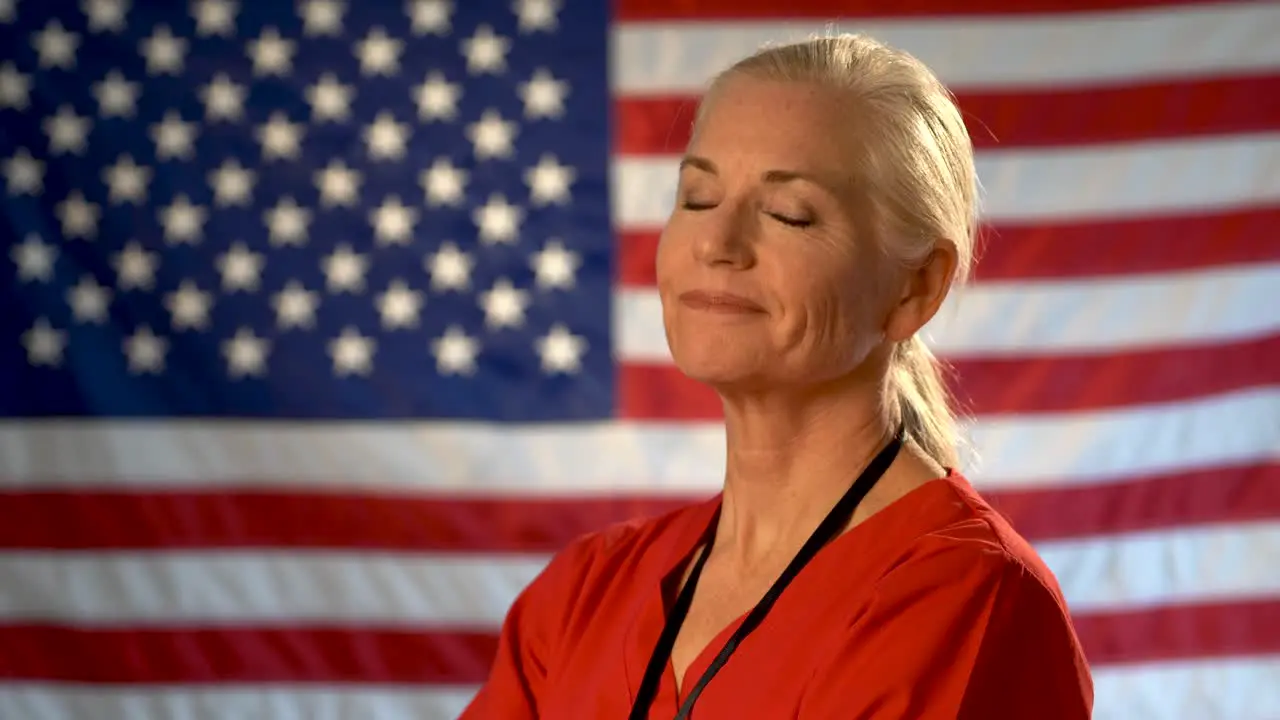 Medium tight portrait of the back of blonde nurses head as she turns quickly and smiles and nods head yes with out of focus American flag