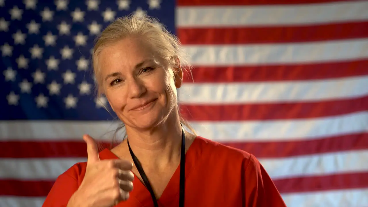 Female nurse walking from out of focus US flag to a medium tight portrait looking very relieved and happy