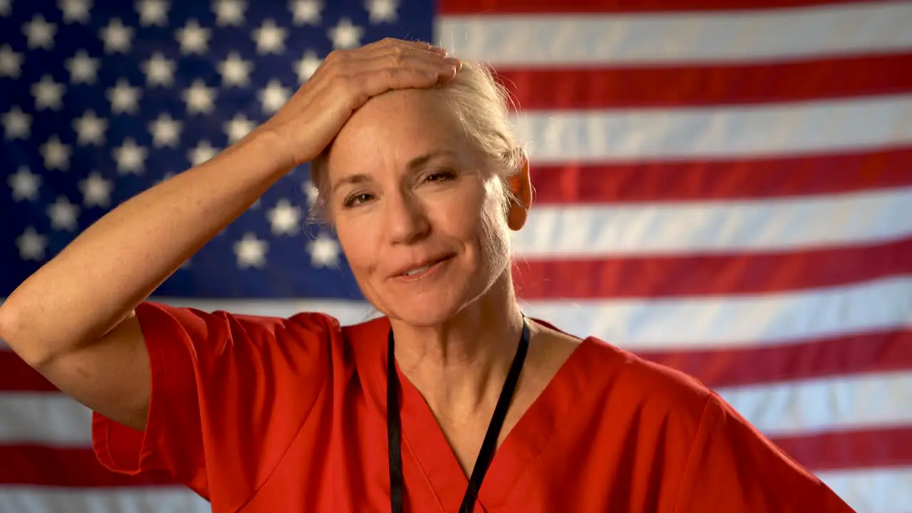 Medium tight portrait of nurse looking at the camera relieved and very happy with a US flag behind her