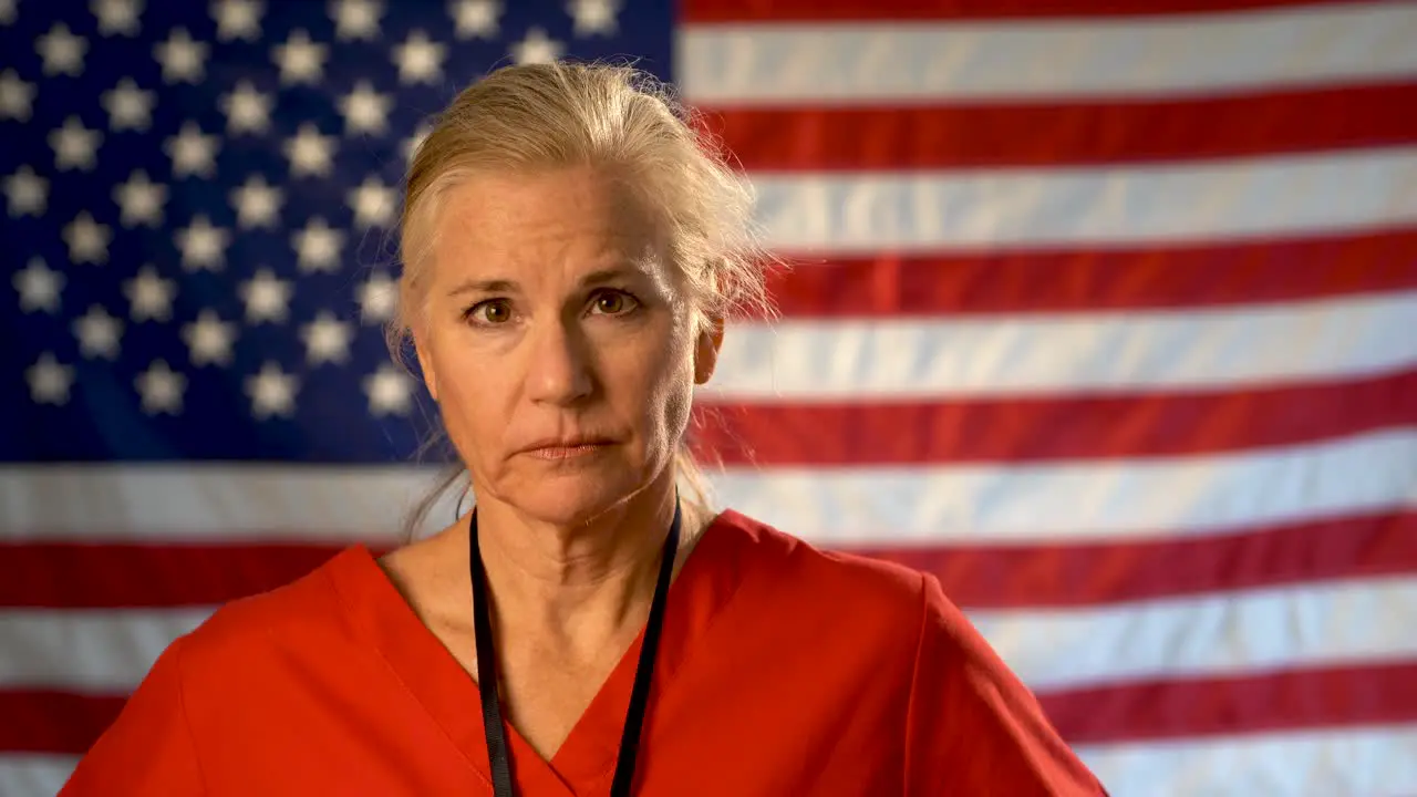 Female nurse walking from out of focus US flag to a medium tight portrait looking very sad worried and concerned