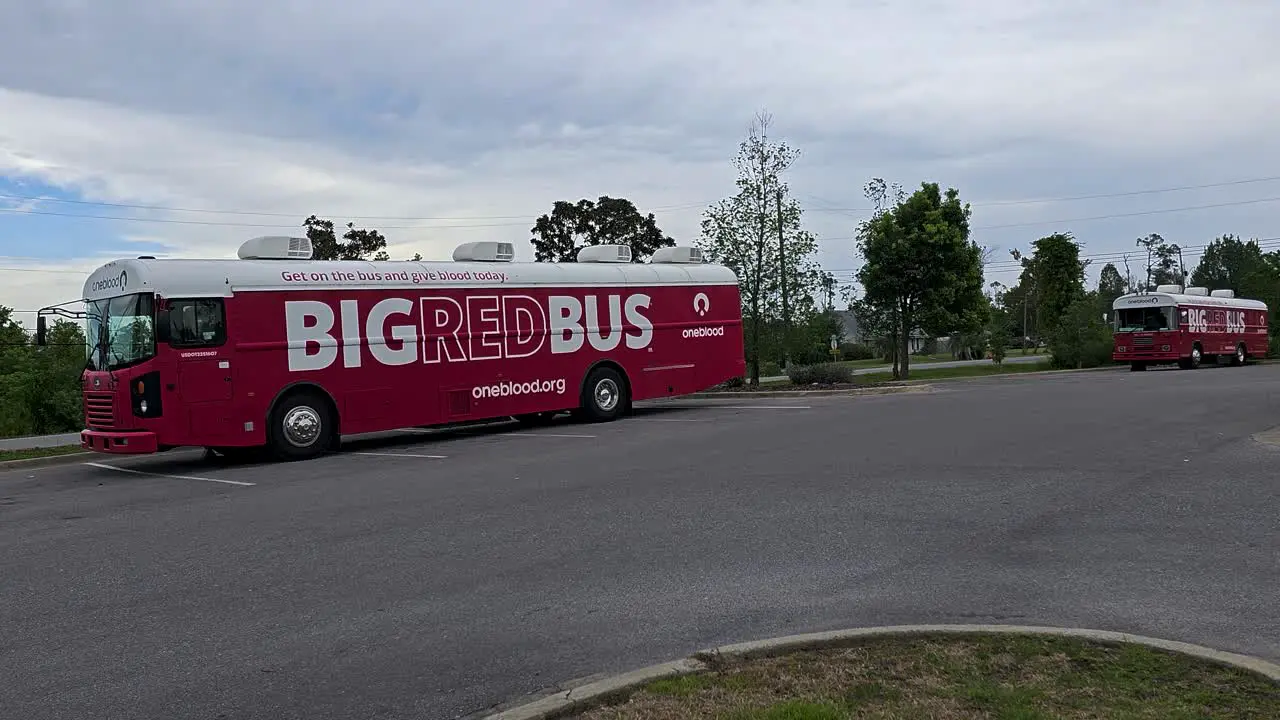 Oneblood big red bus blood donation vehicles sit in parking lot behind facility