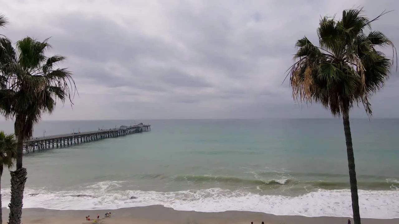 An aerial drone shot flying over San Clemente State Beach California towards the San Clemente Pier on a cloudy day