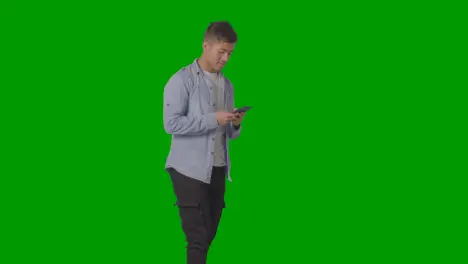 Studio Shot Of Casually Dressed Young Man Checking Mobile Phone Against Green Screen 1