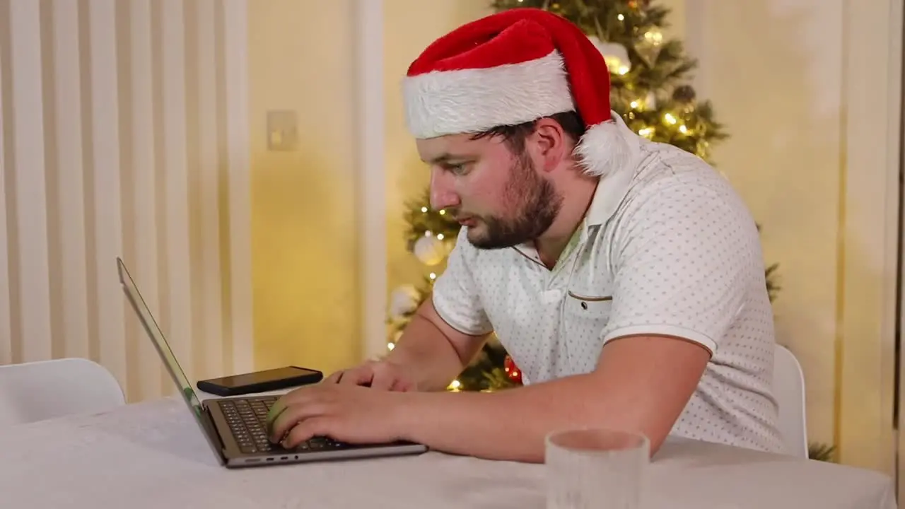 caucasian entrepreneur businessman working from home with a Santa hat during xmas holiday typing on a laptop with a glass of whiskey near a Christmas tree