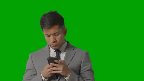 Portrait Of Serious Businessman In Suit Against Green Screen Messaging On Mobile Phone 