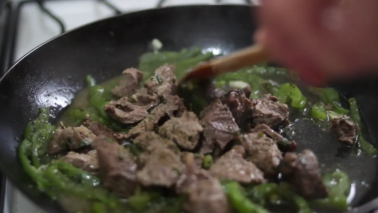 closeup uncovering smoking pan with meat and green pepper stiring with wooden spoon