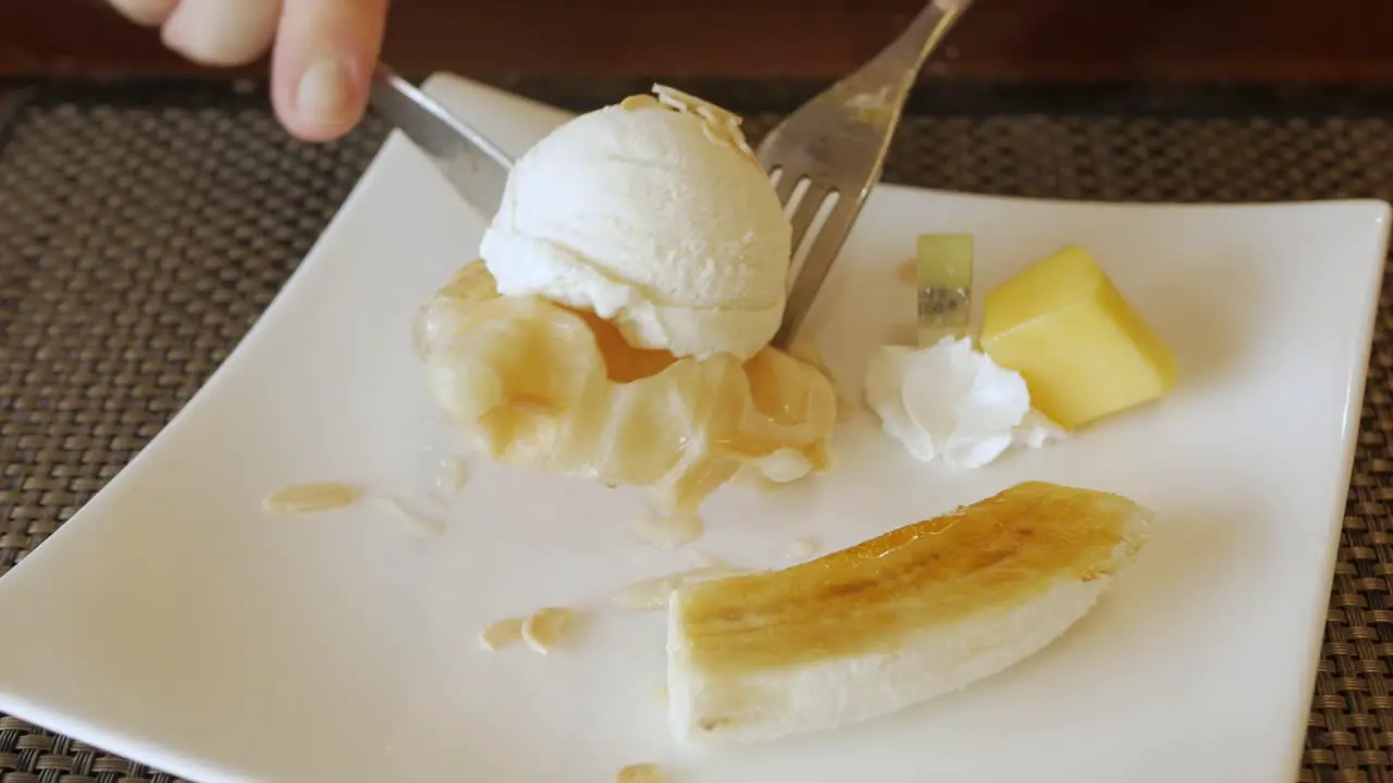 using fork to eat croffle waffles on plate with ice-cream and caramel banana