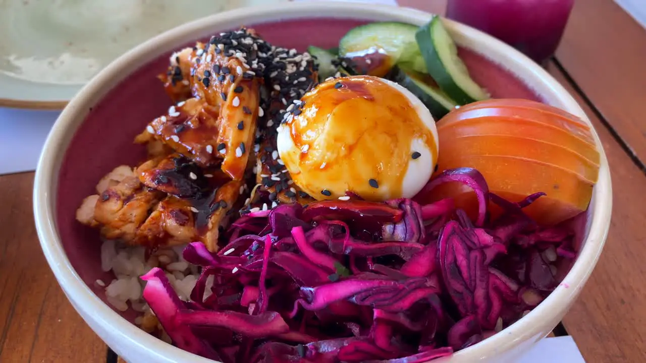 Delicious asian bowl with chicken rice egg purple cabbage tomatoes cucumbers and black sesame seeds at a restaurant 4K shot