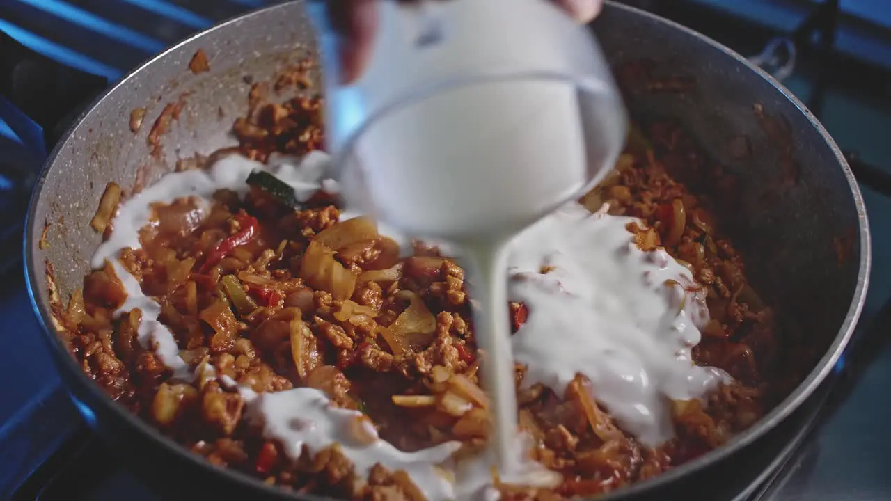 Pouring sauces cream and tomatoes into a wok with meat and vegetables for homemade mexican food close up view