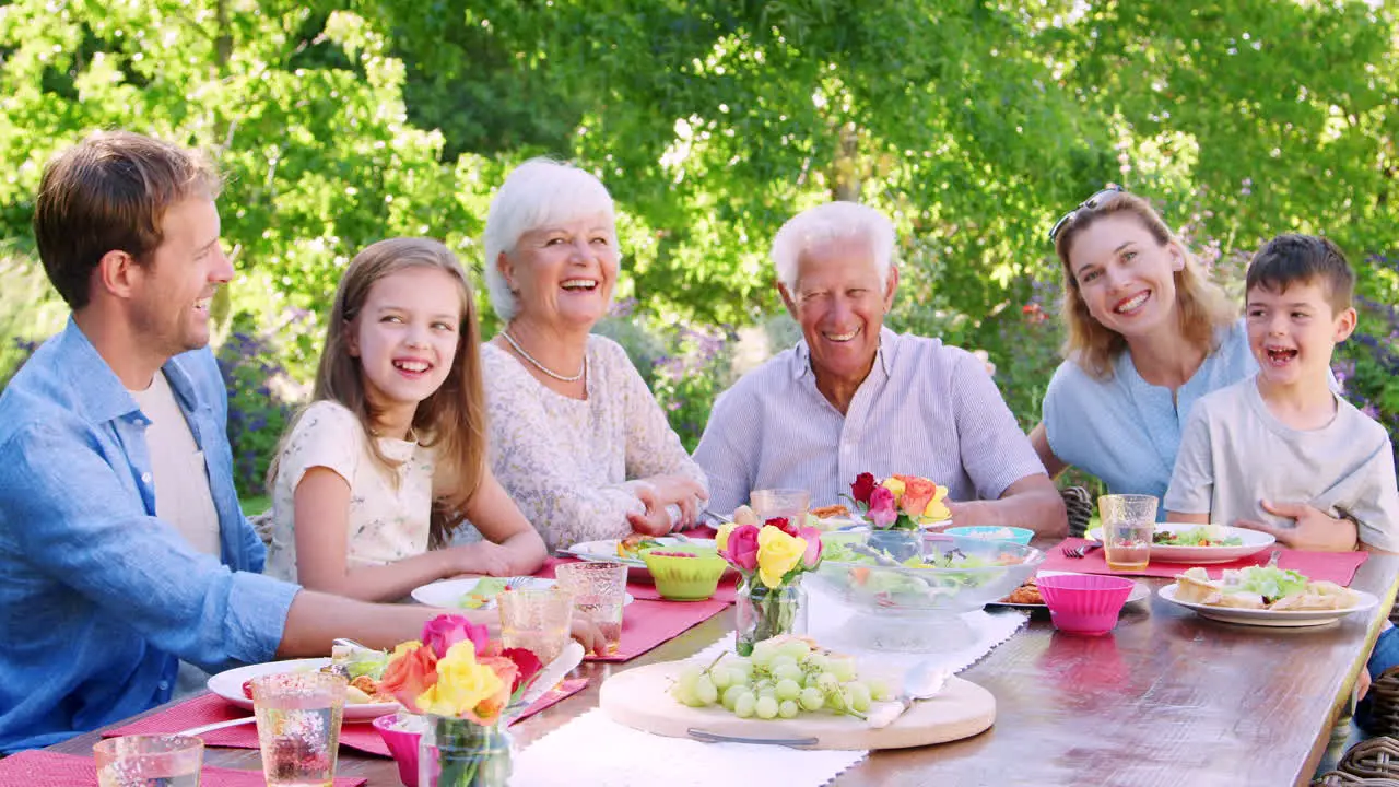 Three generation family at lunch in garden look to camera