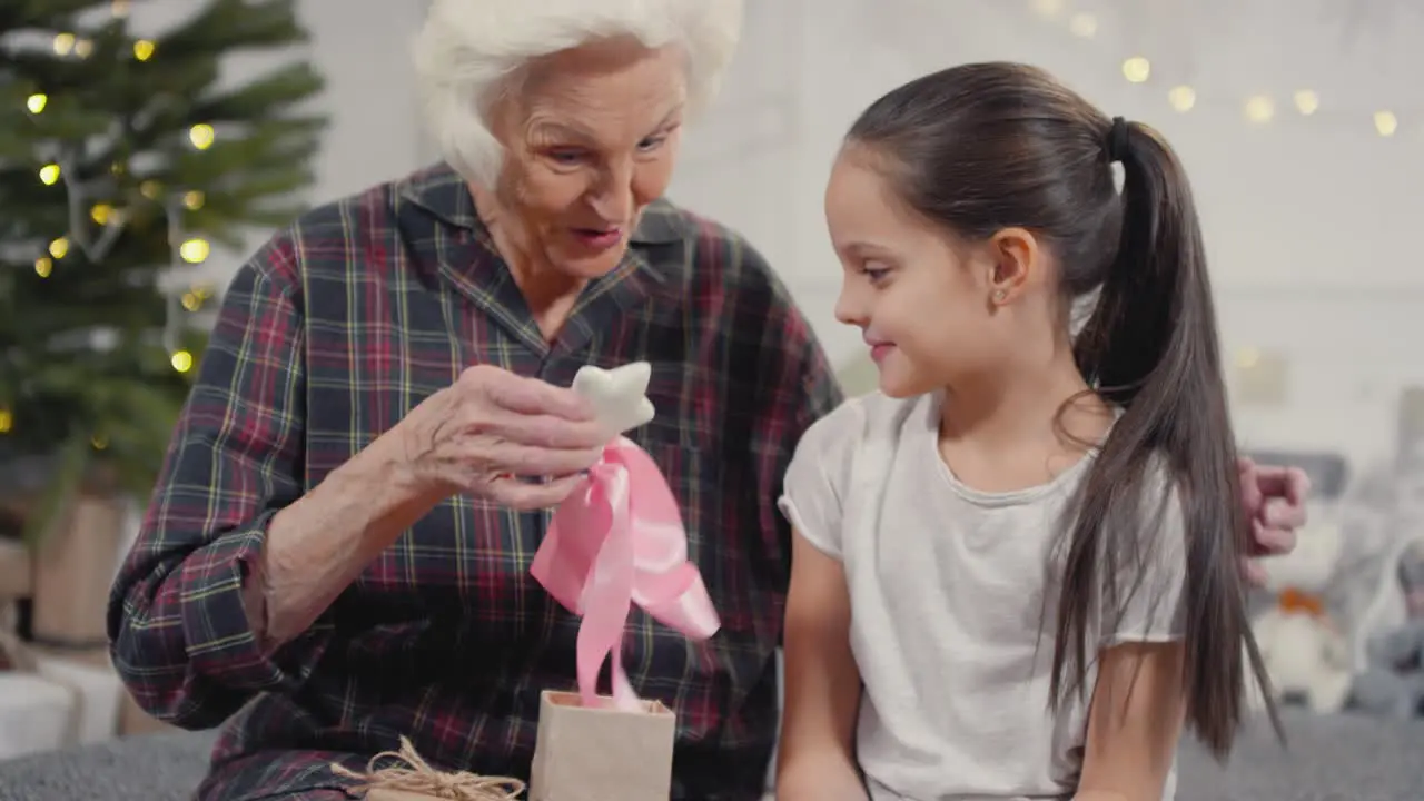 Happy Grandmother Opening Christmas Present From Little Granddaughter And Hugging Her