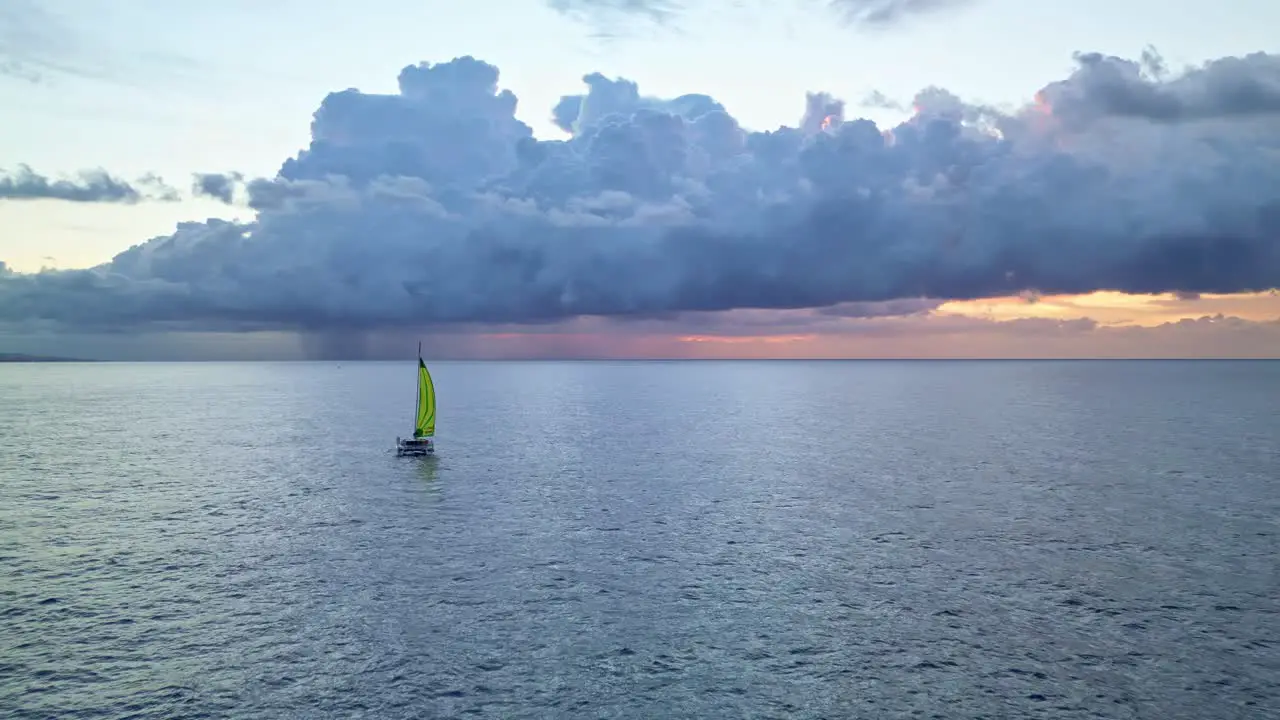 a lone catamaran plying the ocean with a storm formation at sunrise