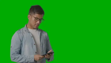 Studio Shot Of Casually Dressed Smiling Young Man Taking Call On Mobile Phone Against Green Screen 3