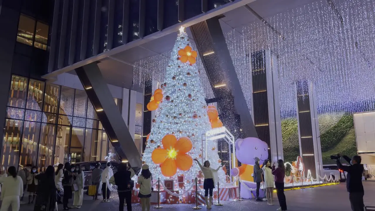 Big white Christmas tree with orange flowers installation near Conrad hotel at night with Chinese people taking photos