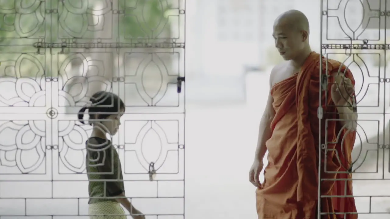 male burmese monk with traditional clothes opening a door to let a female child inside