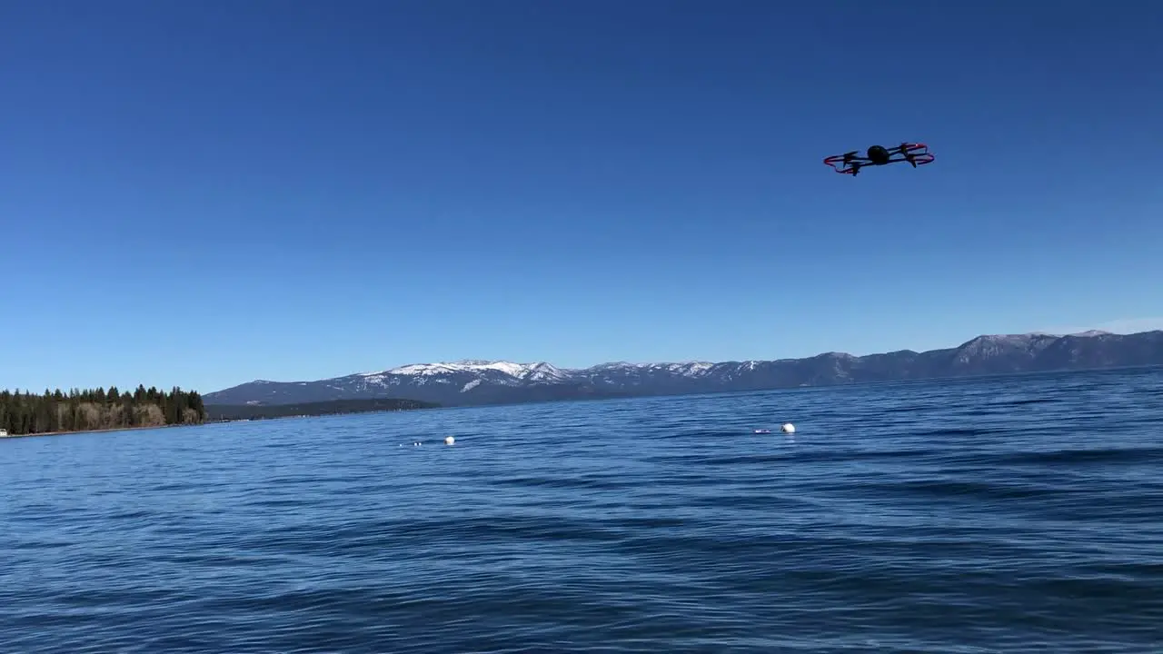 Drone moving up and down in the air with blue sky in the background and water lake below