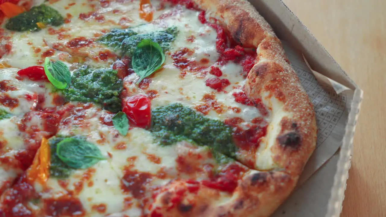 Closeup shot of tasty Neapolitan pizza with pesto sauce in a cardboard pizza box on the table rotating shot