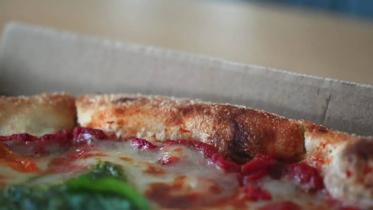 Closeup shot of tasty Neapolitan pizza with pesto sauce in a cardboard pizza box on the table zoom out