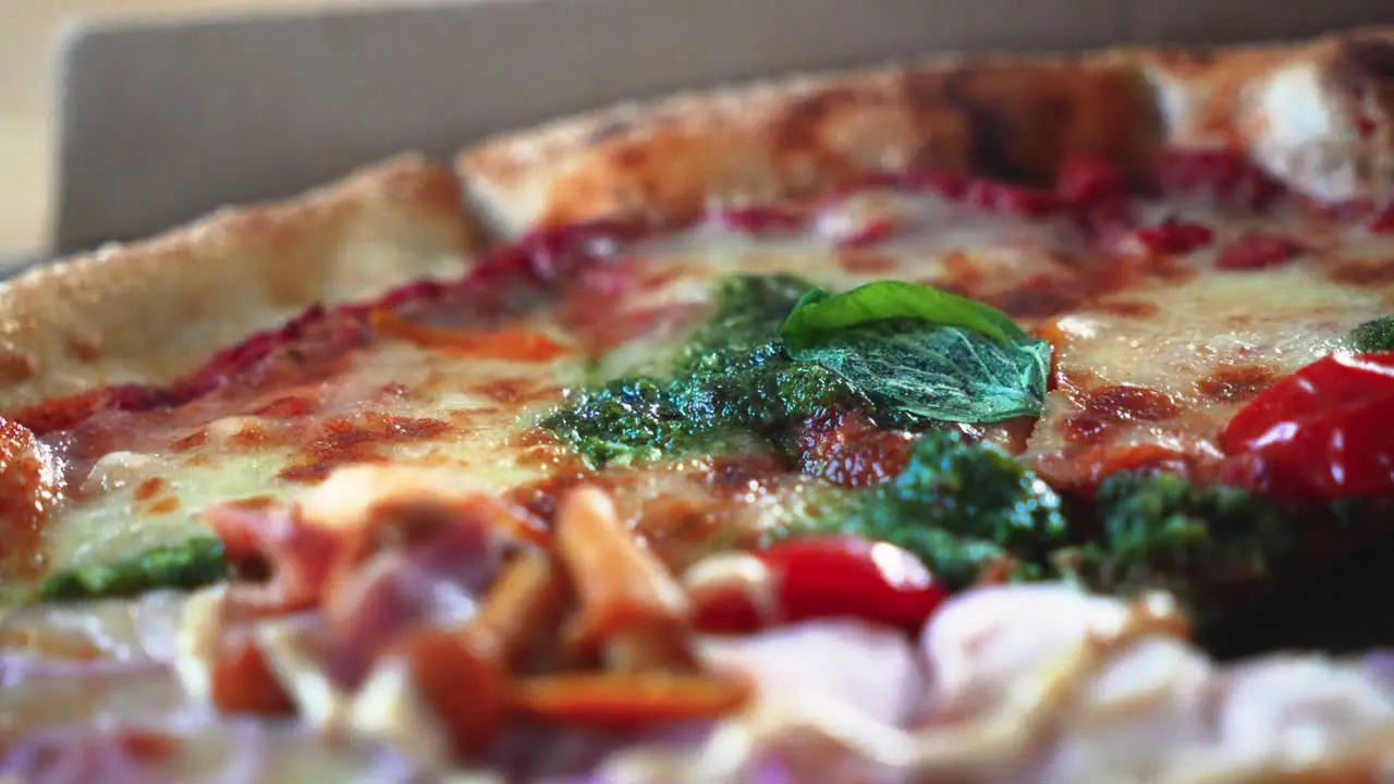 Closeup shot of tasty Italian pizza with pesto sauce in a cardboard pizza box on the table rotating shot