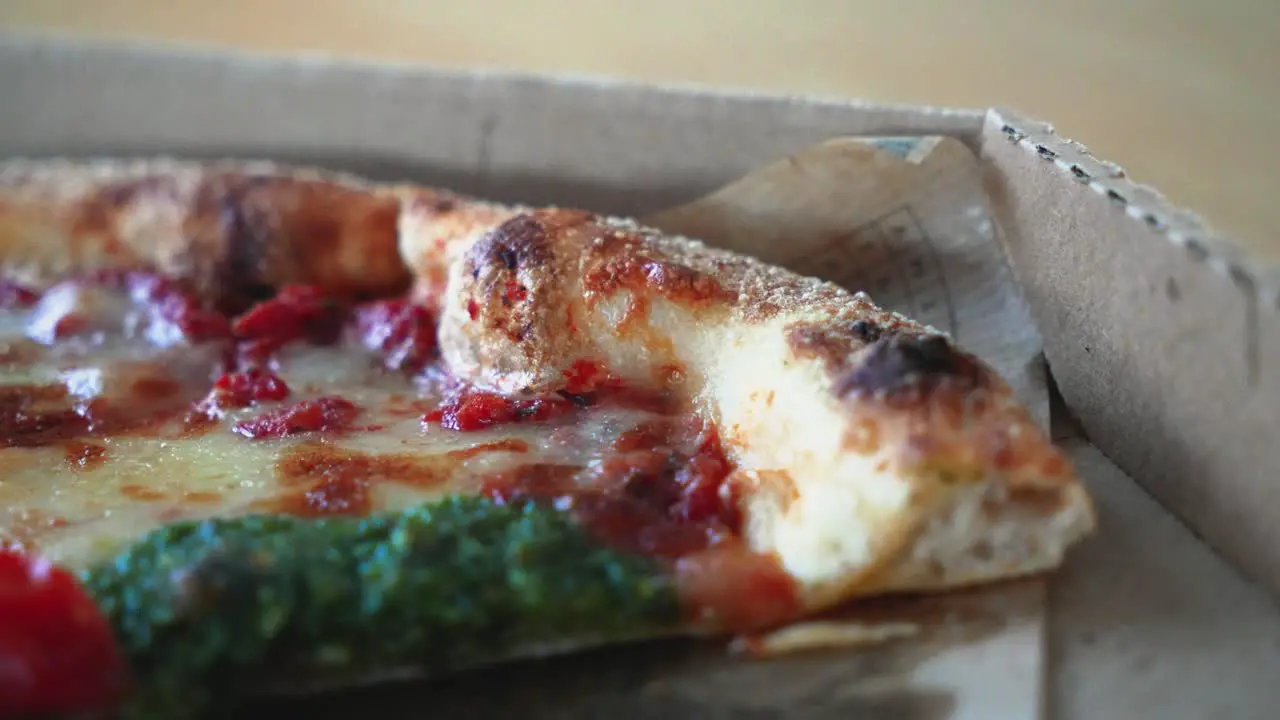 Closeup shot of tasty Neapolitan pizza with pesto sauce in a cardboard pizza box on the table sliding shot