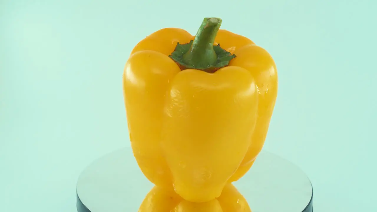 A close up shot of a sweet yellow wet pepper on a reflecting rotating stand 360 slow motion 4k