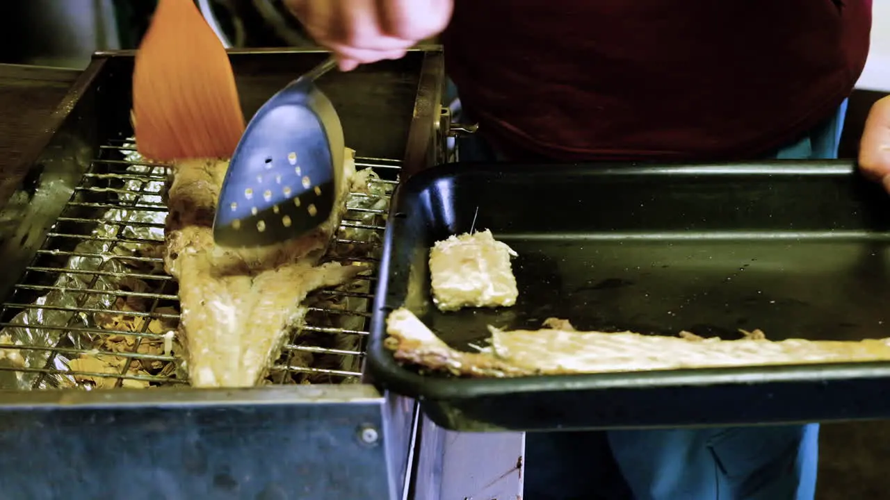 Cooked snoek seafood being moved from smoker with utensils to serving tray