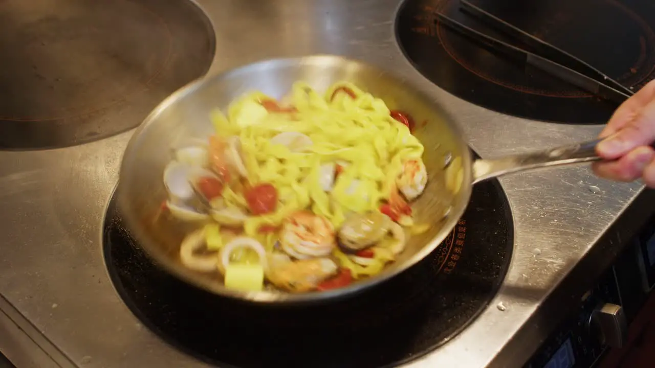 Chef adding butter in a pan with tagliatelle spaghetti with seafood professional restaurant kitchen italian Mediterranean traditional pasta food close up preparation