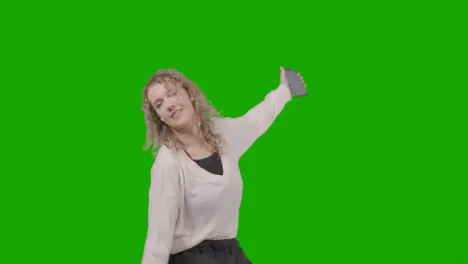 Studio Shot Of Young Woman Listening To Music On Mobile Phone And Dancing Against Green Screen 4