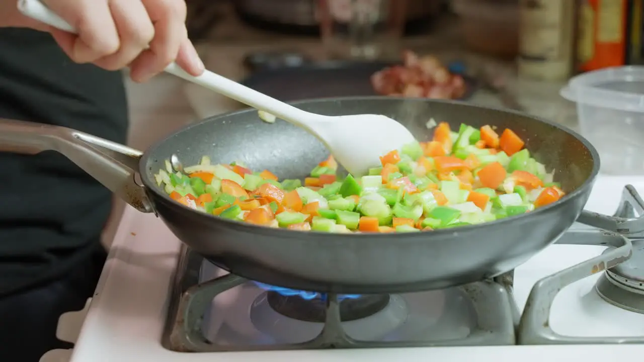 Vegetables being stirred in a frypan by caucasian male hand on gas stove