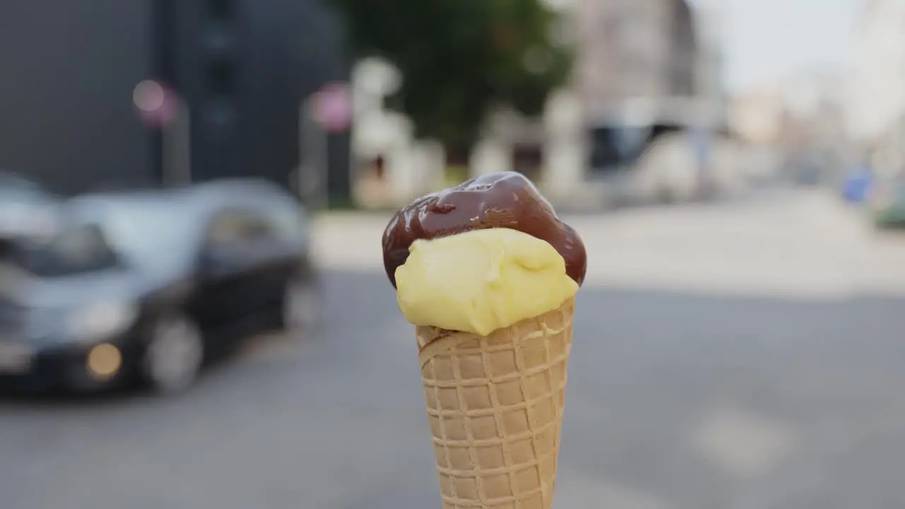 Focused close-up of a vanilla and chocolate ice cream cone being spun by a person on the street