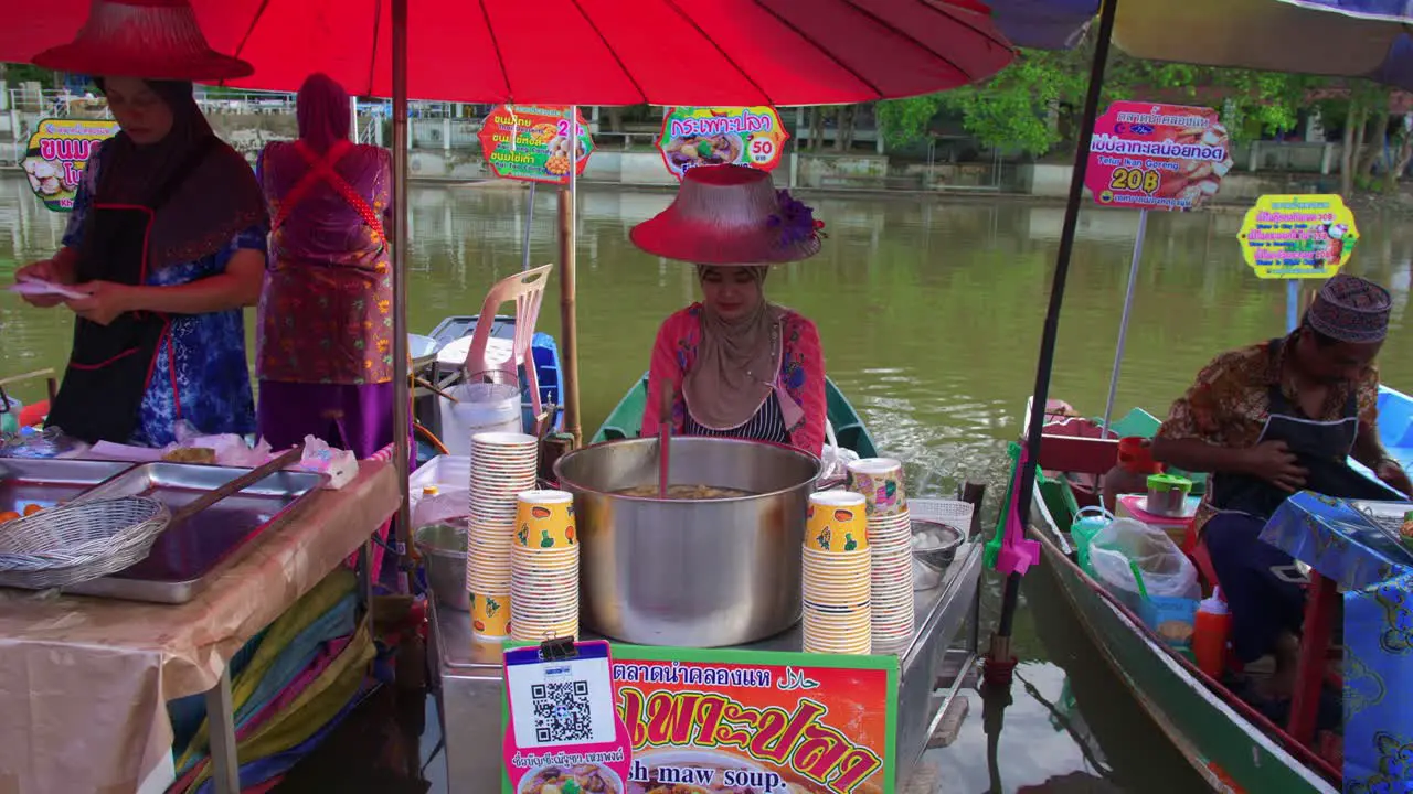 Smiling young Asian worker selling typical Thai food from a boat in a floating market