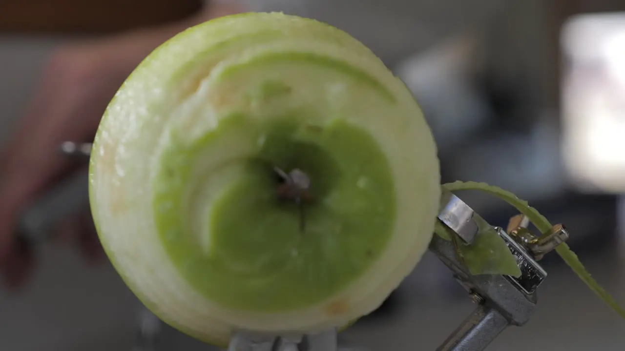 Slow motion front view of green apple being turned and peeled by kitchen device to reveal flesh on bench with juice flying out and low depth of field