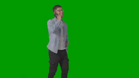 Studio Shot Of Casually Dressed Smiling Man Wearing Glasses Talking On Mobile Phone Against Green Screen 