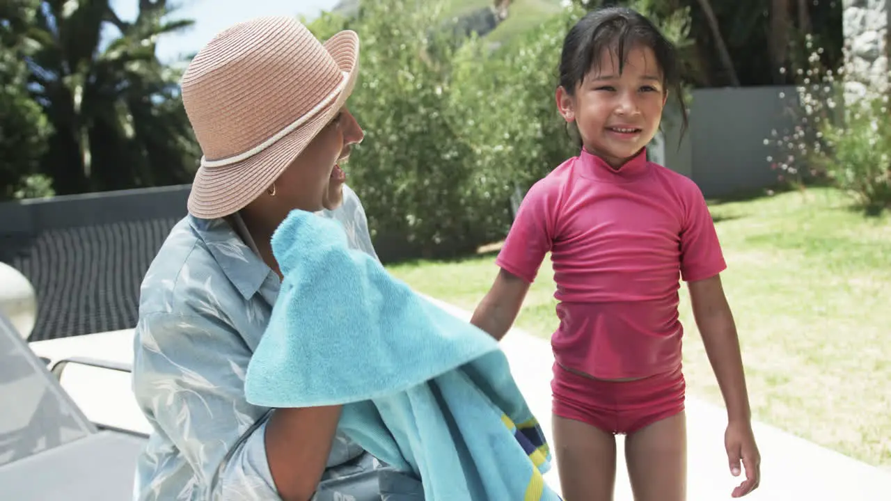 Biracial woman in a sunhat smiles at a biracial girl in a pink swimsuit