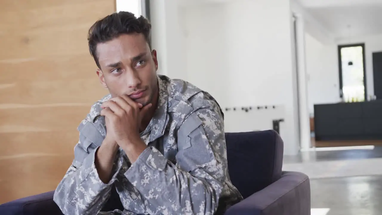 Thoughtful biracial male soldier in uniform sitting in armchair at home slow motion