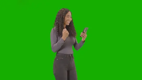 Woman Looking At Mobile Phone And Celebrating Good News Against Green Screen 5