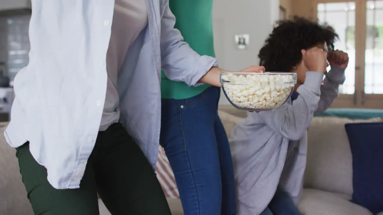 Mixed race lesbian couple and daughter watching tv eating popcorn