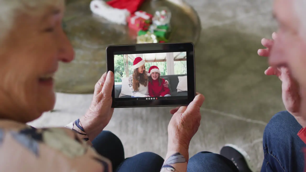 Senior caucasian couple using tablet for christmas video call with happy family on screen