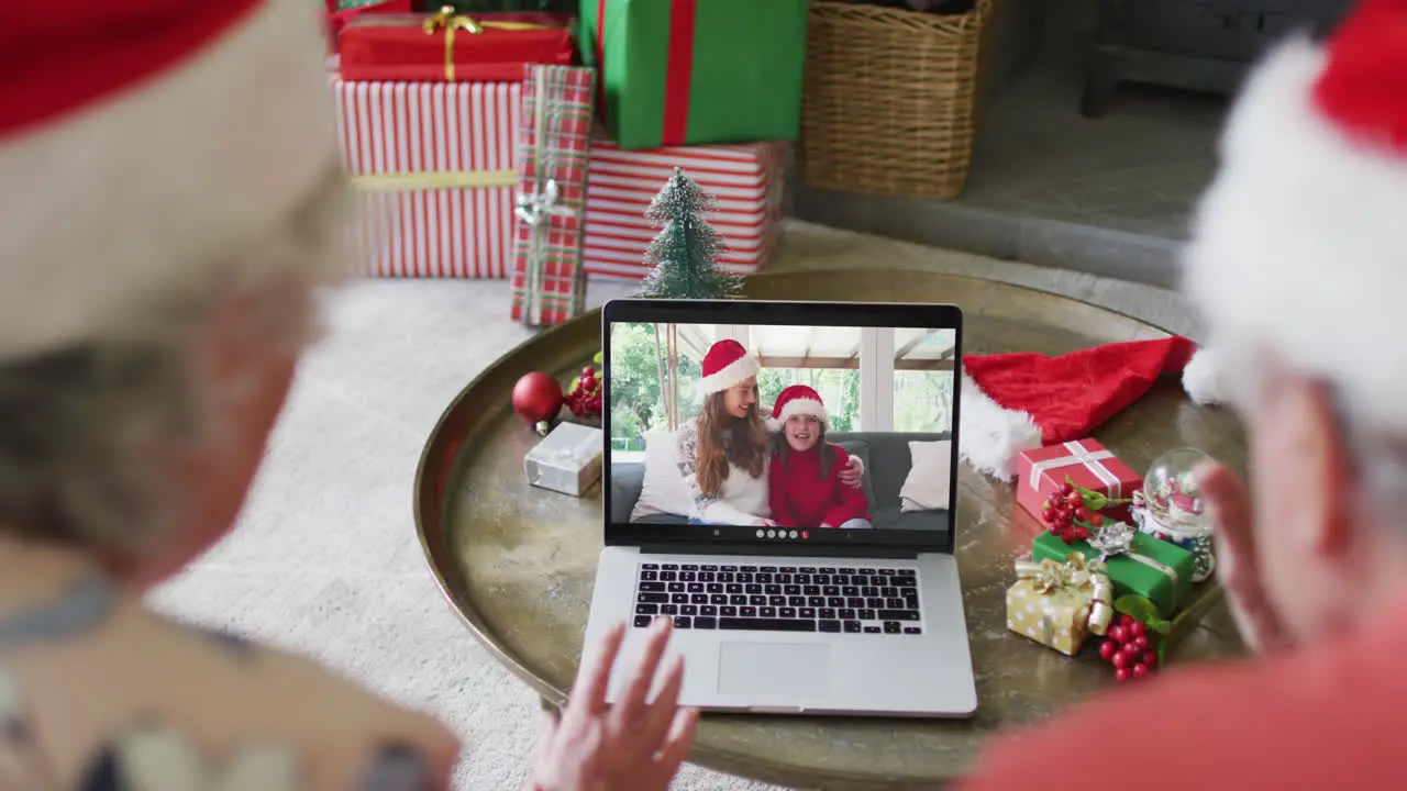 Senior caucasian couple using laptop for christmas video call with happy family on screen