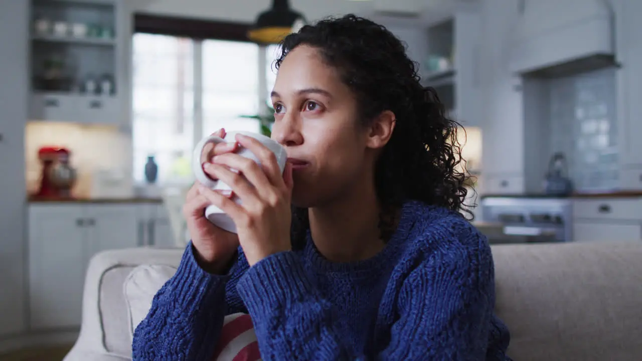 Mixed race woman sitting on couch and drinking coffee