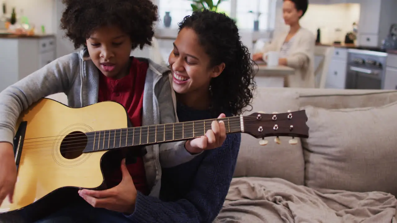 Mixed race mother and daughter sitting on couch playing guitar