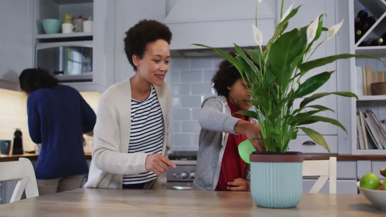 Mixed race lesbian couple and daughter watering plants in kitchen