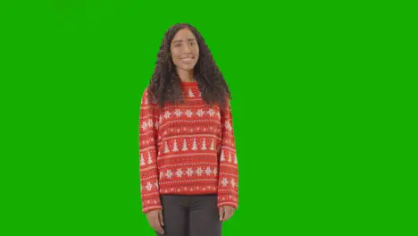 Studio Portrait Of Woman Wearing Christmas Jumper Against Green Screen Smiling At Camera Saying Merry Christmas