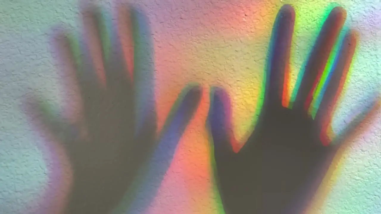 Shadow of two hands casted onto a rainbow colored background