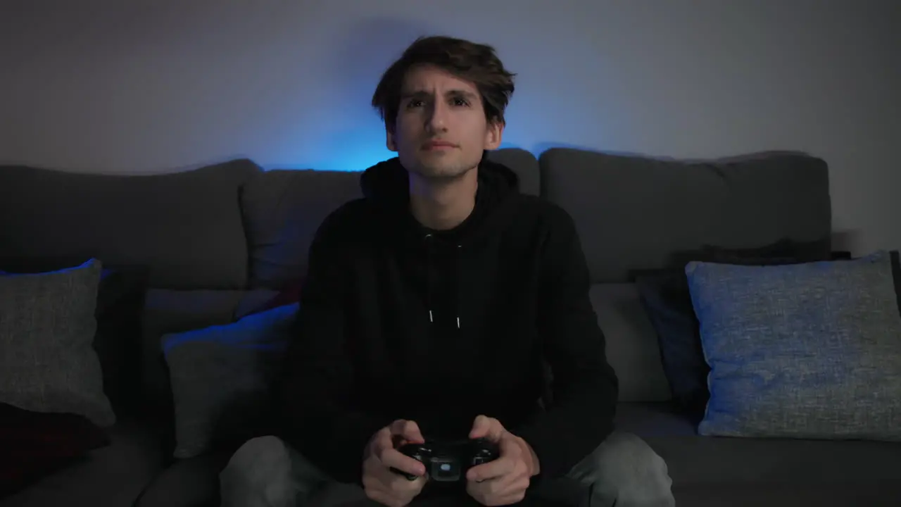 Young Man Playing Video Games At Home With A Blue Light In The Background Medium Shot