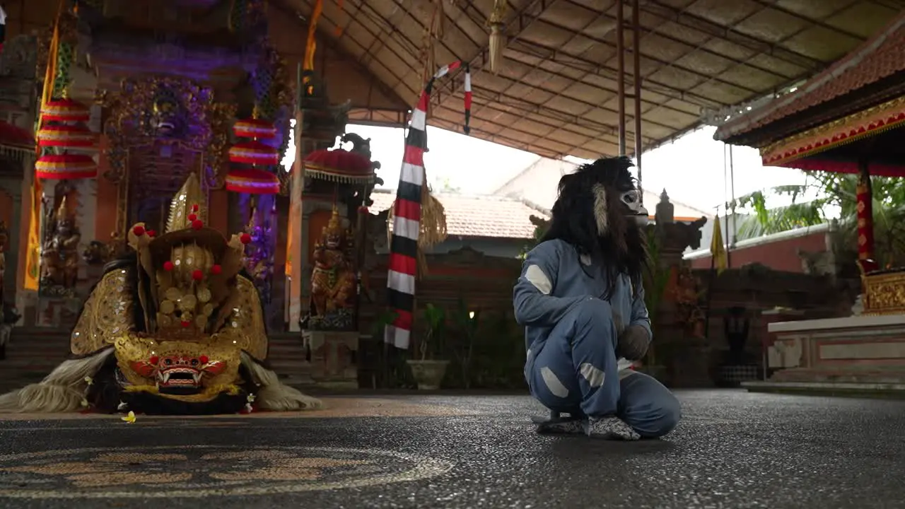 Man in a monkey costume performing in a traditional Bali dance with good and evil characters in front of a dragon in an open air theatre