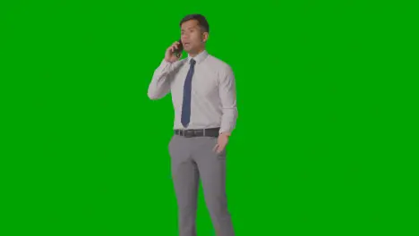 Studio Shot Of Angry Businessman In Suit Talking On Mobile Phone Against Green Screen 