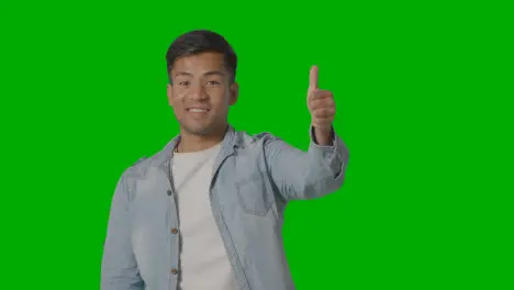 Studio Shot Of Casually Dressed Young Man Giving Thumbs Up Gesture Against Green Screen 