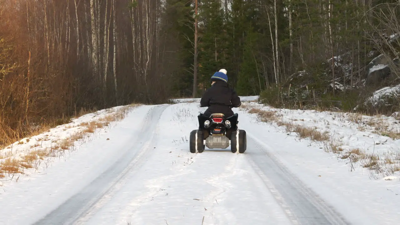 Little Kid drives Quad Bike on deserted road in cold winter forest in Northern Finland