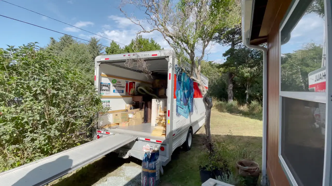 Moving helpers carry boxes out of a U-Haul truck parked close to a residence